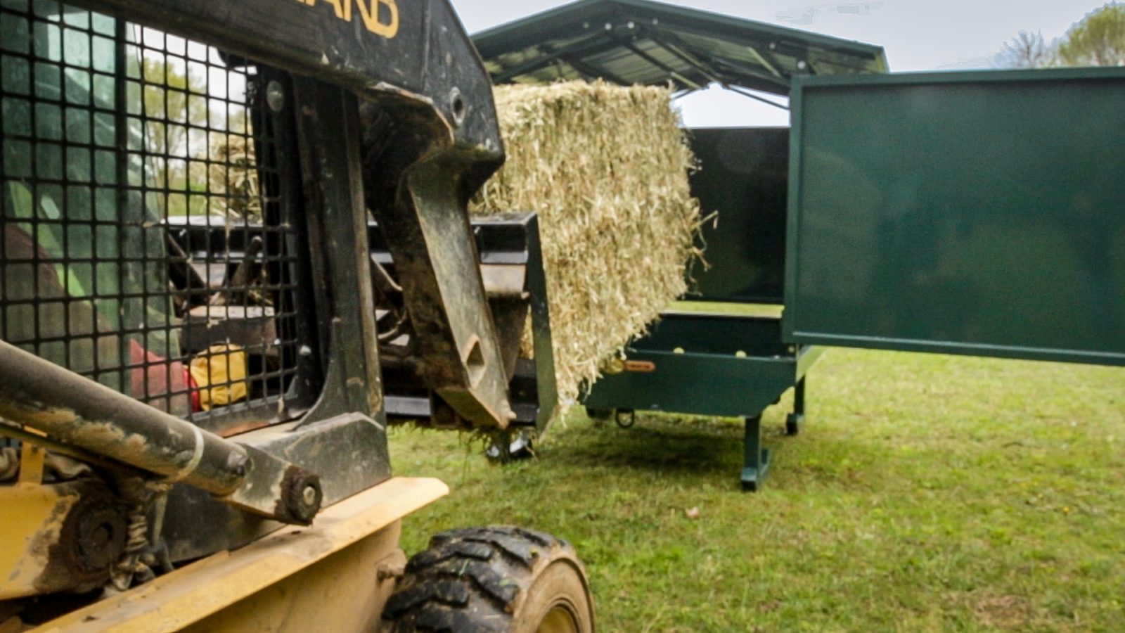 skid loader loading hay on covered hay feeder for horses